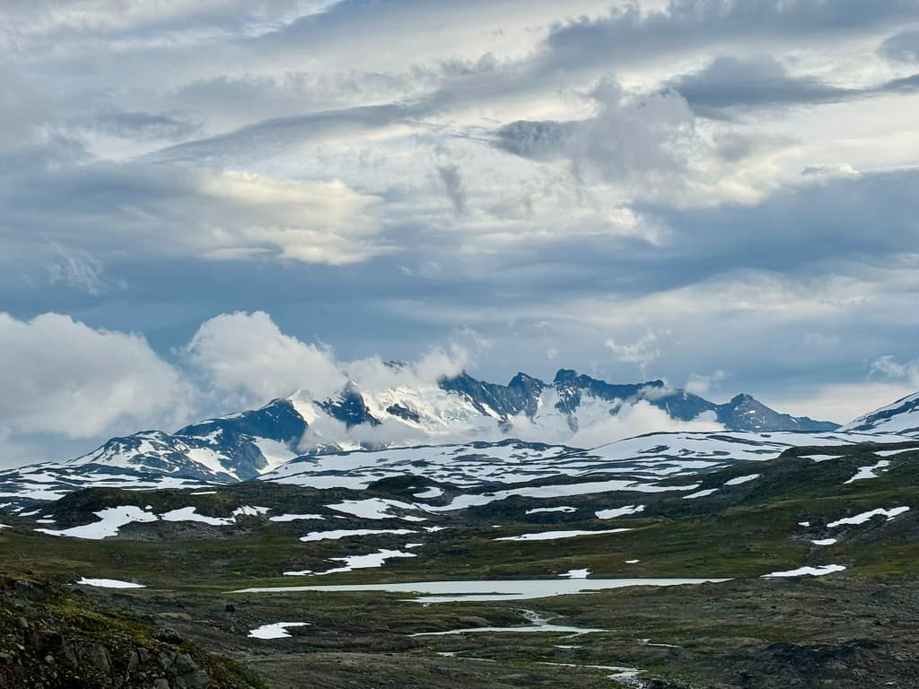 Clouded mountain peaks with snowfields and a tarn in the foreground