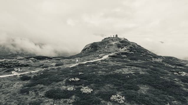 Hiker on a misty ridge path toward a cairn on the summit