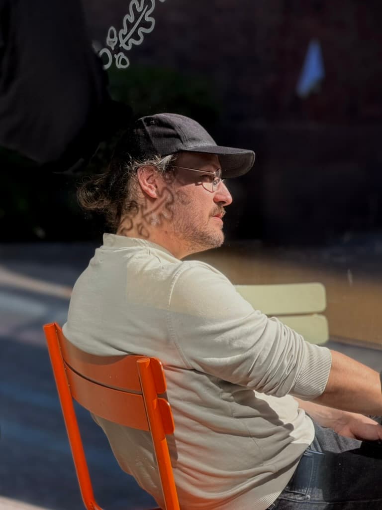 Man in a cap sitting in profile on an orange chair outside a cafe